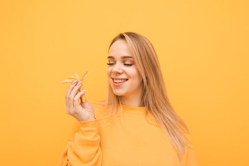 Happy lady in yellow sweatshirt looks at French fries in hand and smiles,isolated on a yellow...