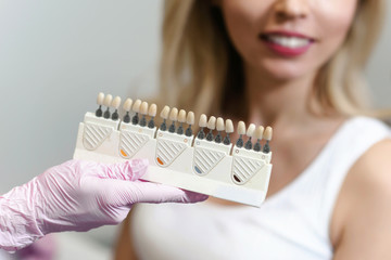 White teeth and beautiful smile of a young woman. Matching the shades of the implants using shade guide. Preparation for teeth whitening in dental office. Closeup macro white background isolated