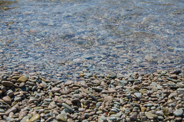 Background of seashore, pebble beach and transparent sea close up