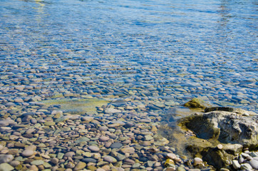 Sea background, ripple surface of transparent water, view of colorful stones bottom underwater