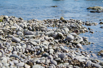 Background of seashore, pebble beach and blue water of sea close up