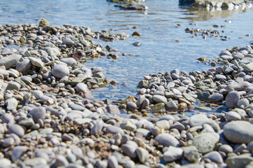 Background of seashore, pebble beach and blue water of sea close up