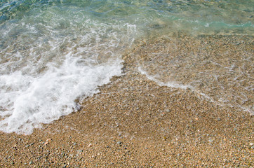Summer background. Colorful coast with sea wave. View of the pebble beach and clear turquoise water