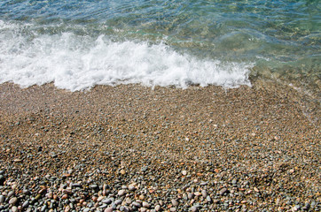 Summer background. Colorful coast with sea wave. View of the pebble beach and clear turquoise water