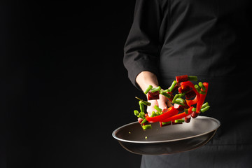 Chef is cooking pepperoni sausages with sweet pepper and spriykovoy beans, on a black background, a...