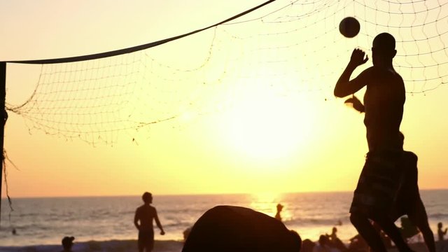 Friends playing beach volleyball at sunset. Concept of sport & health. Summer beach lifestyle. Slow motion.