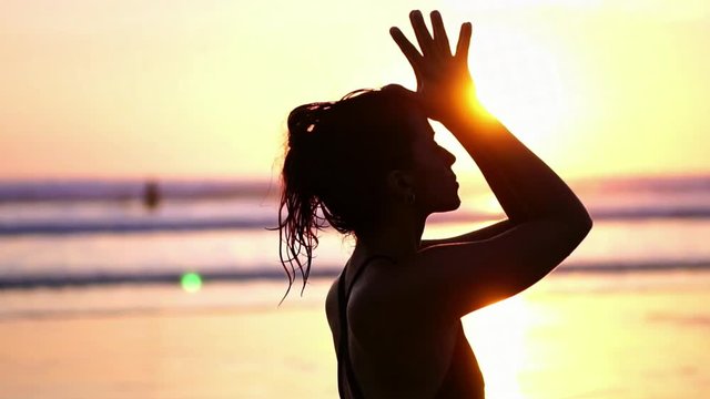 beautiful millennial young fit woman does yoga on the beach at sunset. Slow motion. Concept of healthy living. 