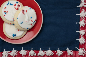 Fototapeta premium white frosted sugar cookies with sprinkles on a red plate and navy with white tassle napkin on red table cloth. Red white and blue are the national colors of many countries.