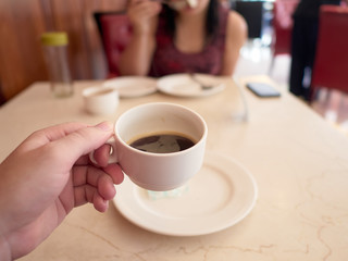 Holding a small cup of coffee in a cafe sitting on a table with another person
