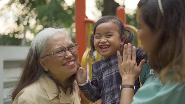 Slow motion of happy little girl kissed by her grandmother and mother on the slide at the park