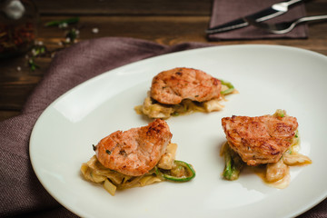 Chicken medallions on a pillow of vegetables. Cafe menu on a wooden background in warm colors with copy space.