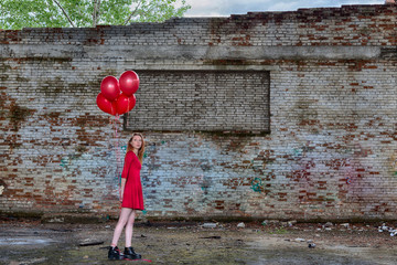 Beautiful young red hair girl in red dress with red helium balloons in hand inside of abandoned...