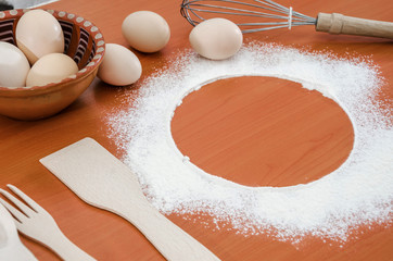 The concept of cooking food. Eggs, wheat flour, whisk and wooden spatula, spoon and fork on the...