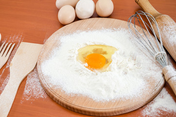 The concept of making dough. Egg chicken  in flour, wooden spatula, whisk and rolling pin on a...