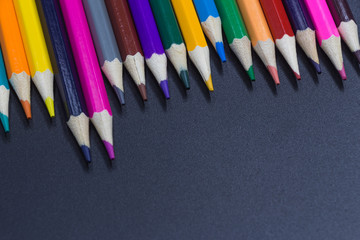 A row of irregularly arranged colored pencils placed on a black background board