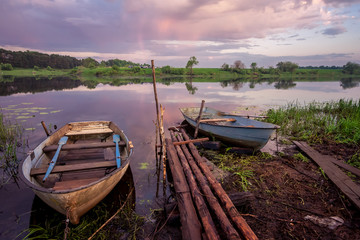 Obraz premium Picture of a row boat on Russian river Nerl on sunset. Blue sky and amazing clouds