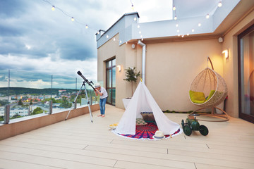 young kid looking in telescope while playing games on rooftop patio
