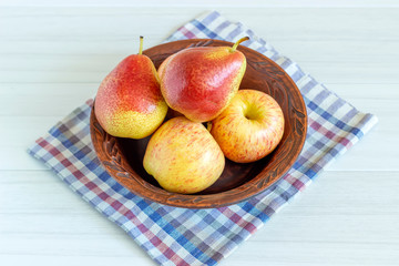 Red pears and apple in brown plate on white wooden table.