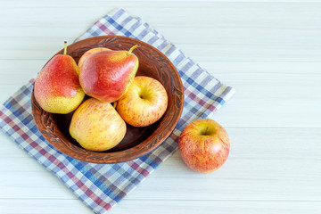 Red pears and apple in brown plate on white wooden table.