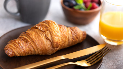 Close up of fresh baked croissant on wooden plate with gold cutlery. Typical ingredient for breakfast in cafe or restaurant.