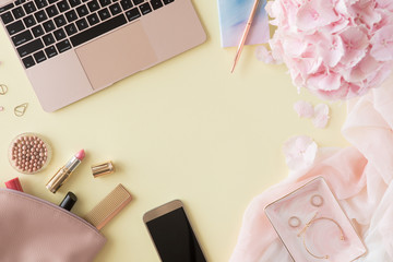 Top view of woman beauty working desk with computer keyboard and laptop, notebook, decorative cosmetic, flowers and palm leaves, envelope on pink and white pastel table. Flat lay background.