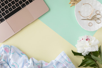 Top view of woman beauty blogger working desk with computer keyboard and laptop, notebook, decorative cosmetic, flowers and palm leaves, envelope on pink and white pastel table. Flat lay background.