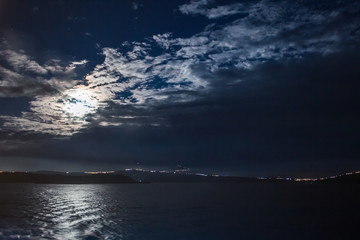 Fototapeta premium Moon partially hidden by clouds over the island of Salamina