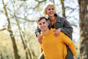 Funny couple in a urban park. Boyfriend carrying his girlfriend on piggyback.