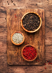 Black, white and pink rose peppers in bowls, assorted spices and spicy herbs on wooden rustic kitchen table, copy space, top view