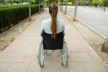 Young girl in wheelchair seen from behind. Outdoors, in a park