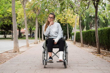 Obraz premium Caucasian young girl with goggles on a wheelchair. Injured sad girl in a park.