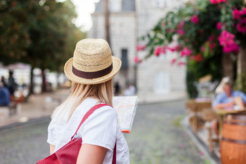 Girl traveler with city map is searching italian authentic street restaurant. Woman tourist is exploring locations, walking in old town. Concept of travel, summer vacation, female tourism, adventure
