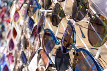 Closeup of colorful sunglasses with dark glasses on a white display rack in summer. Image with selective focus.