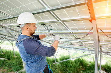 Installing and wiring of stand-alone solar photo voltaic panel system. Close-up of young electrician in hard-hat connecting electrical cables inside the solar modules. Alternative energy concept.