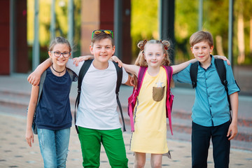 Children's friendship. Four little school students, two boys and two girls, stand in an embrace on...