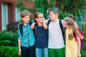 Children's friendship. Four little school students, two boys and two girls, stand in an embrace on the schoolyard.