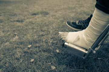 Seen from above a feet in a wheelchair. Foot with sprain on grass bottom