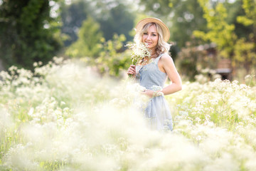 Female portrait outdoors. a woman in a straw hat in a flower field with a bouquet of wild flowers. Summer in the country