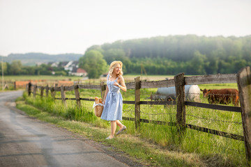 village girl with a bag of milk and bread going through the fields with grazing cows. Summer rural life in Germany. Farming.