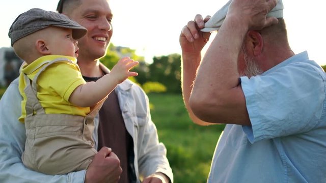 Grandfather and father look at the month-old baby with love. Newborn baby with his grandfather and father on vacation on the river bank. Sunset