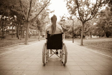Naklejka premium Young girl in wheelchair seen from behind. Outdoors, in a park
