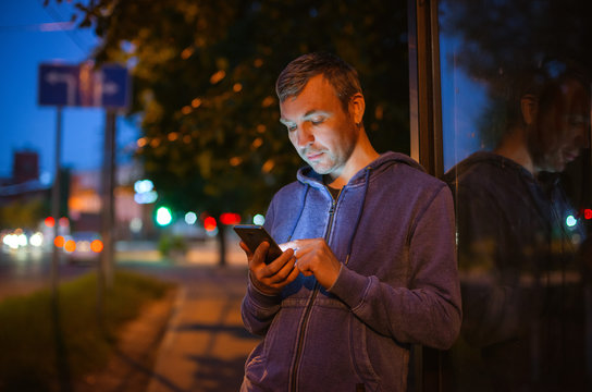 Hipster Man Talking On A Mobile Phone At Night In The City Against The Background Of Bokeh Lights.