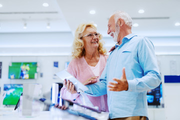 Obraz premium Happy smiling senior choosing new tablet while standing in tech store.