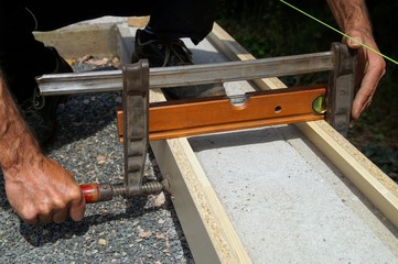 Foundation and form work. Male hand screwing a clamps tool to join planks for a form base. A concrete foundation to build a carport.