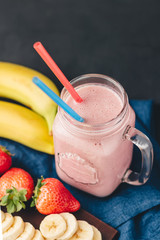 Smoothie with strawberry and banana in the jar at dark background