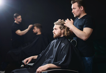 Barbershop concept. Handsome hairdresser cutting hair of male client. Hairstylist serving client at barber shop.