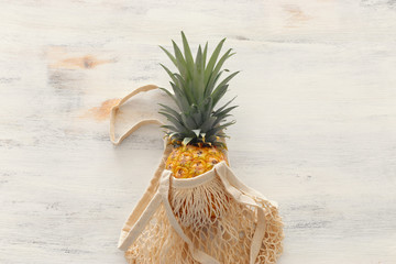 shopping bag with pineapple over white wooden background. Beach and tropical theme. Top view