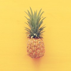 Ripe pineapple over yellow wooden background. Beach and tropical theme. Top view