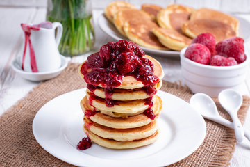 Pancakes with strawberry and jam on plate on white wooden background