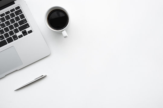 White office desk table with laptop computer, cup of coffee and pen. Top view with copy space, flat lay.